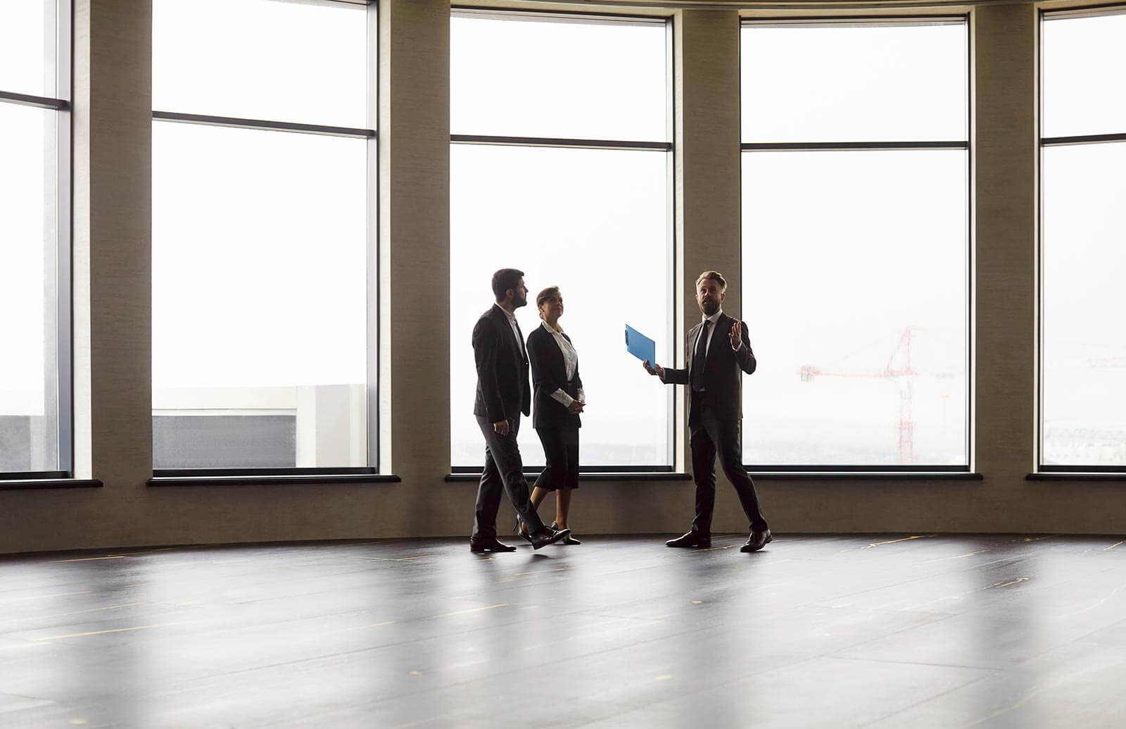 Real estate broker meeting clients inside of large commercial with tall windows